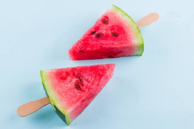 Karpuz dilimi turkuaz bir arka plan üzerinde açılır. Tahta çubuklar üzerinde tatlı karpuz. Yaz konsepti