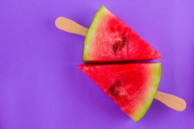 Karpuz dilimi mor bir arka plan üzerinde açılır. Tahta çubuklar üzerinde tatlı karpuz. Yaz konsepti