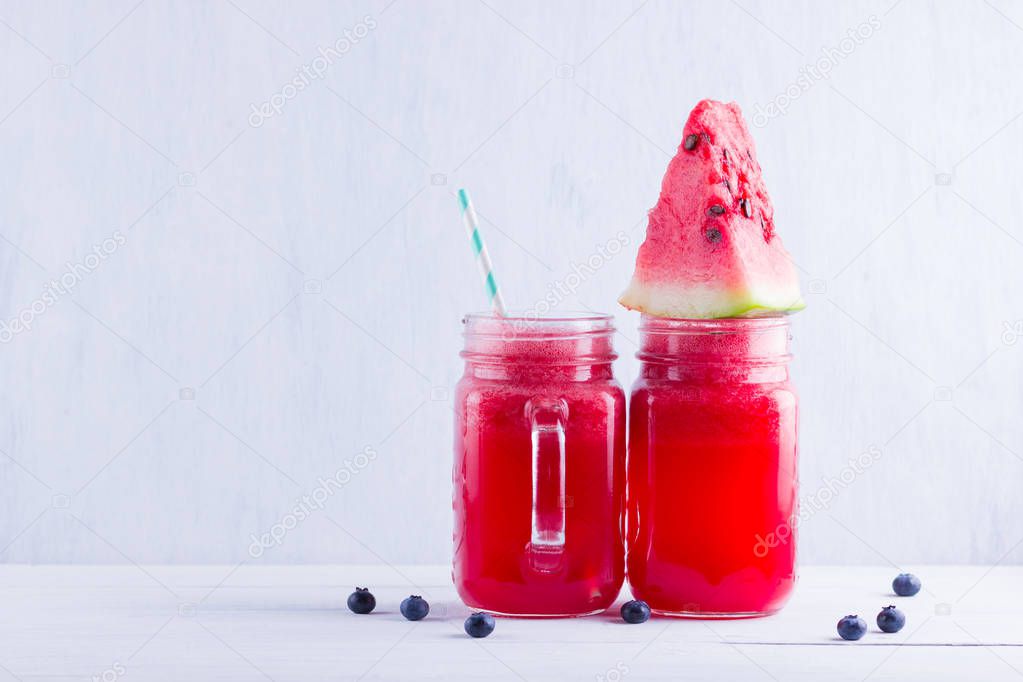 Watermelon drink in mason jars with slices of watermelon. Watermelon smoothies and blueberries on white background. Summer healthy drink for vegetarian. Copy space