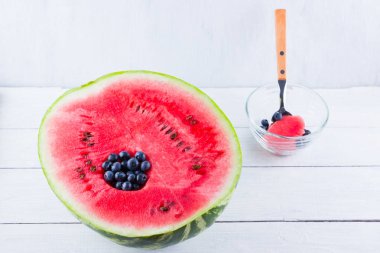 Beyaz arka planda karpuz ve yaban mersini. Bir kaşıkla karpuz yeme işlemi. Karpuzda yaban mersini. Yaratıcı gıda konsepti