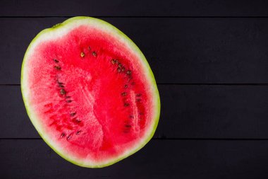 Karpuzun yarısı koyu zeminde. Tahta tahtalarda dilimlenmiş karpuz. Vegan için sağlıklı bir besin. Üstte görüntü