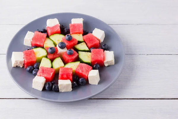 Watermelon salad with feta cheese. Healthy salad with blueberries, cucumbers, watermelon and cheese. Summer salad on gray plate