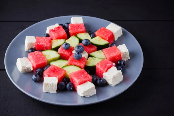 Watermelon salad with feta cheese. Healthy salad with blueberries, cucumbers, watermelon and cheese. Summer salad on dark background