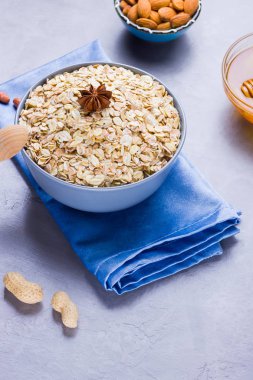 Kuru yulaf ezmesi, fındık ve bal. Yulaf ezmesi ve badem fıstığı çimento arka plan üzerinde. Sağlıklı kahvaltı yapmak için tahıl ve fıstık. Mavi peçete üzerinde kase yulaf ezmesi