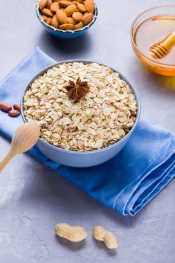 Kuru yulaf ezmesi, fındık ve bal. Yulaf ezmesi ve badem fıstığı çimento arka plan üzerinde. Sağlıklı kahvaltı yapmak için tahıl ve fıstık. Mavi peçete üzerinde kase yulaf ezmesi