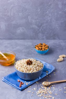 Kuru yulaf ezmesi, fındık ve bal. Yulaf ezmesi ve badem fıstığı çimento arka plan üzerinde. Sağlıklı kahvaltı yapmak için tahıl ve fıstık. Mavi peçete üzerinde kase yulaf ezmesi