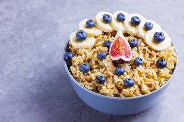 Sağlıklı kahvaltı. Yabanmersinli yulaf ezmesi, muz ve incir. Meyve ve böğürtlenli yulaf ezmesi. Çimento arka planında pişmiş yulaf ezmesi. Boşluğu kopyala