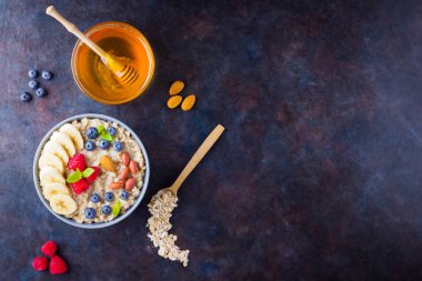 Sağlıklı kahvaltı. Meyveli, fındıklı ve ballı yulaf ezmesi. Yabanmersinli yulaf ezmesi, muz ve ahududu. Koyu arkaplanda pişmiş yulaf ezmesi. Vejetaryen yemeği.