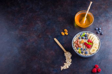 Sağlıklı kahvaltı. Meyveli, fındıklı ve ballı yulaf ezmesi. Yabanmersinli yulaf ezmesi, muz ve ahududu. Koyu arkaplanda pişmiş yulaf ezmesi. Vejetaryen yemeği.