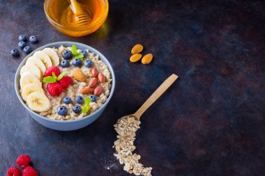 Sağlıklı kahvaltı. Meyveli, fındıklı ve ballı yulaf ezmesi. Yabanmersinli yulaf ezmesi, muz ve ahududu. Koyu arkaplanda pişmiş yulaf ezmesi. Vejetaryen yemeği.