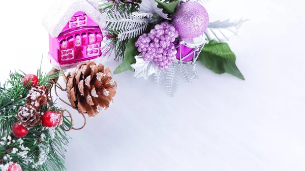 Holiday decorations on fir branch. Christmas decorations on white background. Pine cone and red berries on fir branch. Purple ball and colorful toy houses. Widescreen