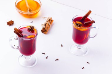 Baharatlı sıcak şarap ve beyaz arka planda bal. Noel şarabı, portakal, anason ve tarçınlı. İki bardak kış Noel içkisi.