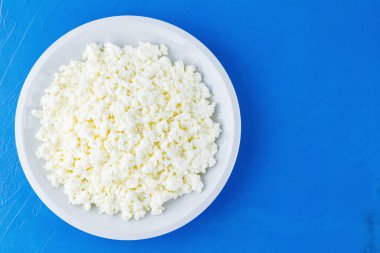 Mavi arka planda beyaz tabakta süzme peynir. Organik ekolojik sağlıklı yemek, süt ürünleri. Bir tabak ev yapımı süzme peynir. Üst Manzara. Boşluğu kopyala