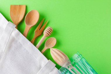 Sıfır atık. Yeşil arka planda pamuk eko çanta, cam ve ahşap çatal bıçak. Çevre dostu ahşap çatal bıçak seti. Plastiksiz konsept. Minimalizm. Üst Manzara. Boşluğu kopyala