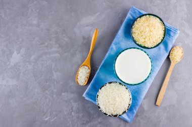 Gri arka planda pirinç ve süt tohumu. Mavi bir peçetede pirinç sütü. Çimento arka planında süt içermeyen vegan. Yükselişten gelen alternatif süt. Minimalizm. Boşluğu kopyala
