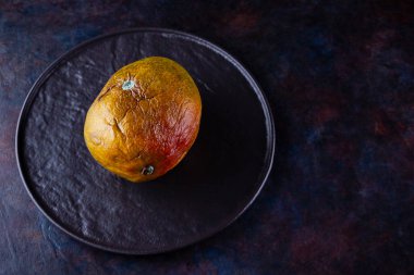 Çirkin mango. Karanlık arka planda bozulmuş mango. Siyah tabakta çürük mango. Üst Manzara. Boşluğu kopyala