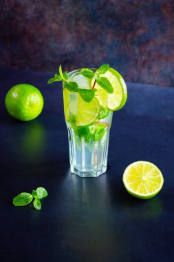 Limonlu mojito kokteyli ve uzun bardakta nane şekeri. Koyu arkaplanda cam içinde taze mojito. Naneli kokteyli limonla tazeliyorum. Erimiş su.