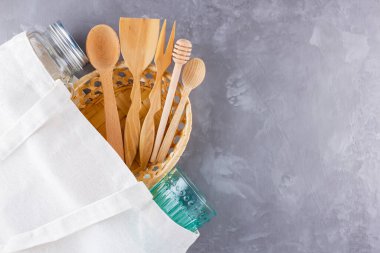 Sıfır atık. Pamuk çanta, cam ve gri arka planda tahta çatal bıçak. Çevre dostu ahşap çatal bıçak seti ve mason kavanozu. Plastiksiz konsept. Minimalizm. Üst Manzara. Boşluğu kopyala