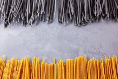 Gri arka planda siyah ve sarı makarna. Çimento arka planında sarı ve siyah spagetti. Çiğ spagetti bolonez. Yemek geçmişi konsepti. Üst görünüm