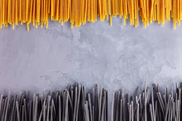 Gri arka planda siyah ve sarı makarna. Çimento arka planında sarı ve siyah spagetti. Çiğ spagetti bolonez. Yemek geçmişi konsepti. Üst görünüm