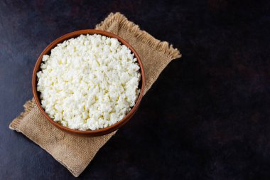 Çuval bezinde süzme peynir. Koyu bir arka planda taze süzme peynir. Siyah arka planda yumuşak peynir. Minimalizm. Üst Manzara. Boşluğu kopyala