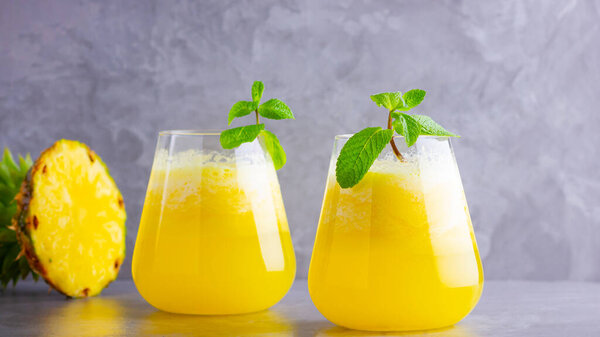 Ананасовый коктейль в двух стаканах на сером фоне. Холодный ананасовый коктейль с мятой. Летний тропический коктейль. Здоровый напиток
