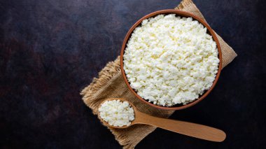 Çuval bezinde süzme peynir. Koyu arkaplanda taze süzme peynir ve ahşap kaşık. Siyah arka planda yumuşak peynir. Üst Manzara. Boşluğu kopyala