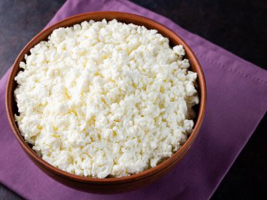 Koyu bir arka planda süzme peynir. Kâsede taze süzme peynir. Keten peçetede yumuşak peynirli kil tabağı. Minimalizm. Üst Manzara. Boşluğu kopyala