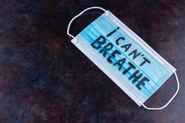 I CAN'T BREATHE on a surgical mask. Protective face mask with "I can't breathe" on a dark background. Concept Black Lives Matter. Copy space. Top view