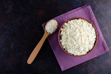 Koyu arkaplanda süzme peynir ve ahşap kaşık. Kâsede taze süzme peynir. Keten peçetede yumuşak peynirli kil tabağı. Üst Manzara. Boşluğu kopyala