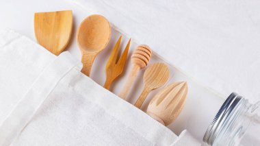 Sıfır atık. Pamuk eko çanta, duvar kavanozu ve beyaz arka planda ahşap çatal bıçak takımı. Çevre dostu ahşap çatal bıçak seti ve beyaz peçete. Plastiksiz konsept. Üst Manzara. Boşluğu kopyala