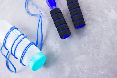 İp atlama ve bir şişe su ile spor konsepti. Gri arka planda spor aletleri. Sağlıklı yaşam tarzı kavramı. Uzayı kopyala Üst görünüm