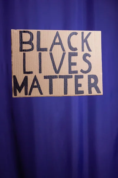 BLACK LIVES MATTER on a blue blurred background. No racism concept. Cardboard banner with a text 