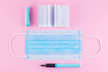 Okul konseptine geri dönelim. Okul not defteri, kalem ve koruyucu maske. Kırtasiye ve yüz maskesi. Karantina döneminde eğitim. Üst görünüm