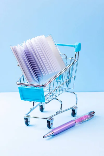 Shopping cart with school supply. School notepad with holographic cover. Notepad and pen in shopping trolley. Back to school concept