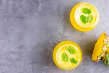 Gri arka planda ananas suyu. Bardakta detoks sıvısı var. Taze ananaslı ananas püresi. Sağlıklı yaz içkisi. Üst Manzara. Boşluğu kopyala