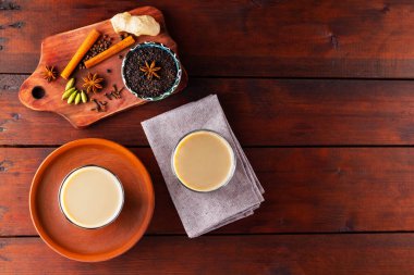 İki bardak Masala çayı ve çeşitli malzemeler. Tahta tahtada Masala çayı. Sütlü çay ve baharat. Uzayı kopyala Üst görünüm