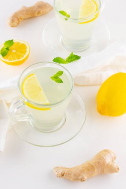 Beyaz peçeteye limonlu zencefil çayı ve nane şekeri. İki fincan zencefilli çay, limon, zencefil kökü ve ballı beyaz arka plan. Üst görünüm