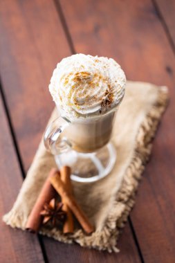 Cam bardakta balkabağı aromalı latte. Balkabaklı latte, çırpılmış krema ve ahşap arka planda baharatlar. Çuval bezinde sıcak sonbahar kahvesi.