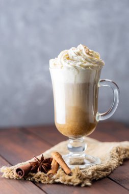 Cam bardakta balkabağı aromalı latte. Balkabaklı latte, çırpılmış krema ve ahşap arka planda baharatlar. Çuval bezinde sıcak sonbahar kahvesi.