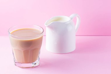 Pembe arka planda sütlü çay. Bir bardak Masala çayı ve süt sürahisi. Pastel arka planda baharatlı çay ve süt. Minimalizm. Boşluğu kopyala