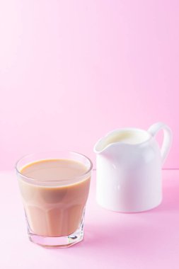 Pembe arka planda sütlü çay. Bir bardak Masala çayı ve süt sürahisi. Pastel arka planda baharatlı çay ve süt. Minimalizm. Boşluğu kopyala