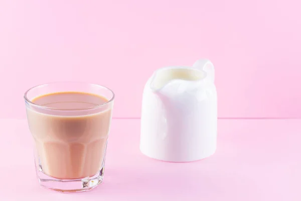 Milk tea on a pink background. Glass of masala chai tea and milk jug. Spiced tea and milk on a pastel background. Minimalism. Copy space