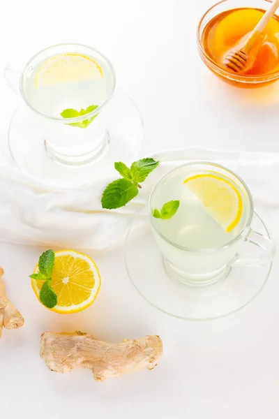 Ginger tea with lemon and mint on a white napkin. Two cups of ginger tea, lemon, ginger root and honey on white background. Top view