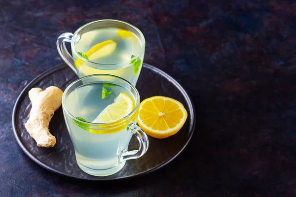 Ginger tea with lemon on a dark background. Two cups of ginger tea on a black plate. Copy space. Top view