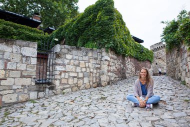 Sıcak yaz gününde tarihi şehrin boş caddesinde oturan güzel turist kız..