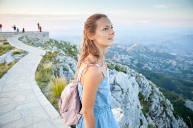 güzel kız turistik bir uçurumun üstünde duruyor ve Karadağ'ın dağ aralığının güzel manzara hayran. Turizm,