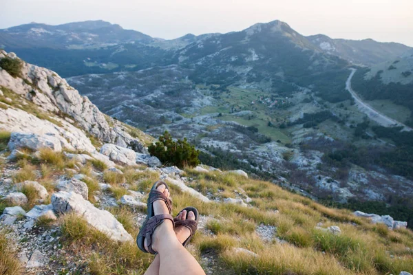 Legs of the traveler in the foreground panoramic view of the green valley of the mountain range, Montenegro