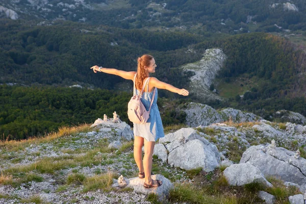 Hermosa chica turística se encuentra en la cima de un acantilado y admira el hermoso paisaje de la cordillera en Montenegro. Concepto de turismo, viajes y vacaciones de verano — Foto de Stock