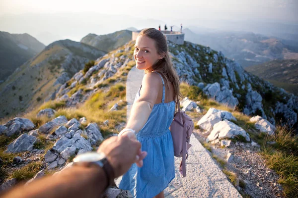 Chica inspirada pasa tiempo con un chico sosteniendo su mano en el fondo de la naturaleza. Jovencita alegre lleva a un amigo a las montañas. Lovcen Montenegro — Foto de Stock